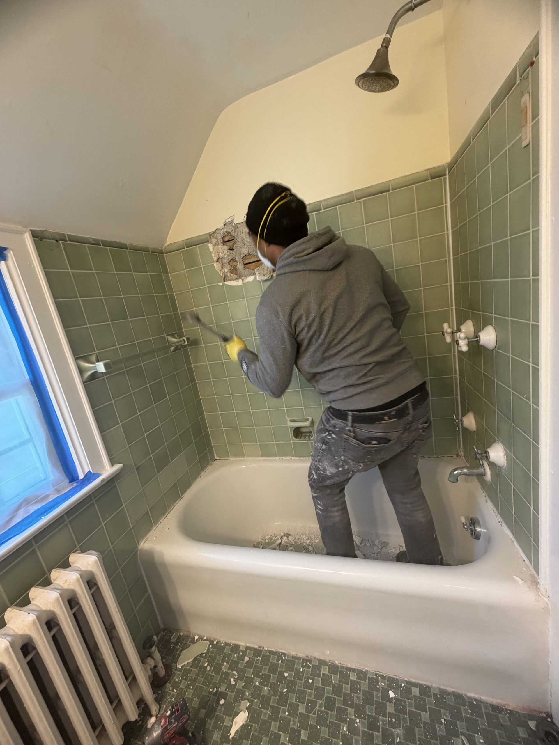 Demolition in progress on cast iron bathtub and green tile shower surround