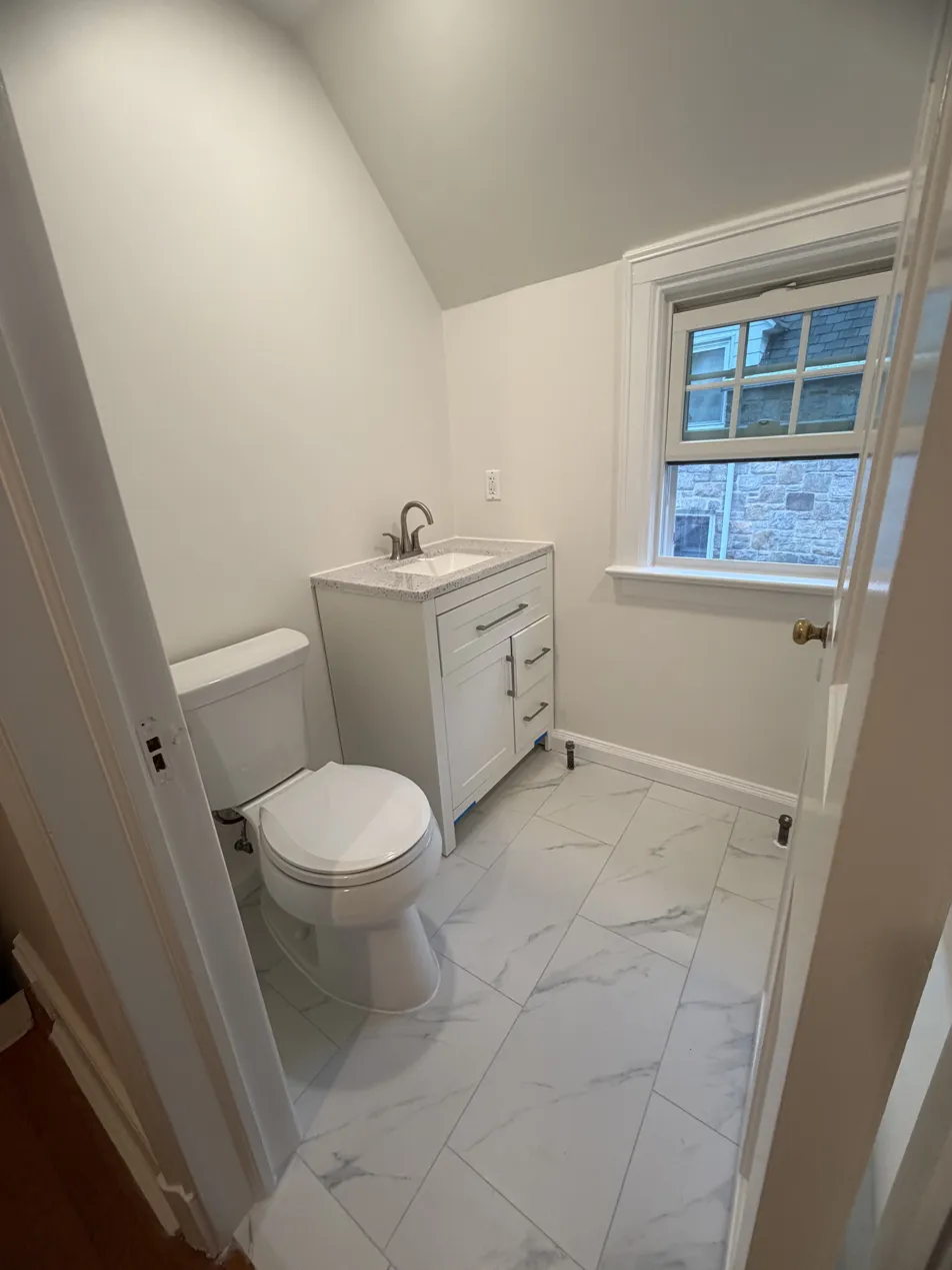 Finished Scarsdale guest bathroom with white vanity, toilet, and marble-look floor tile